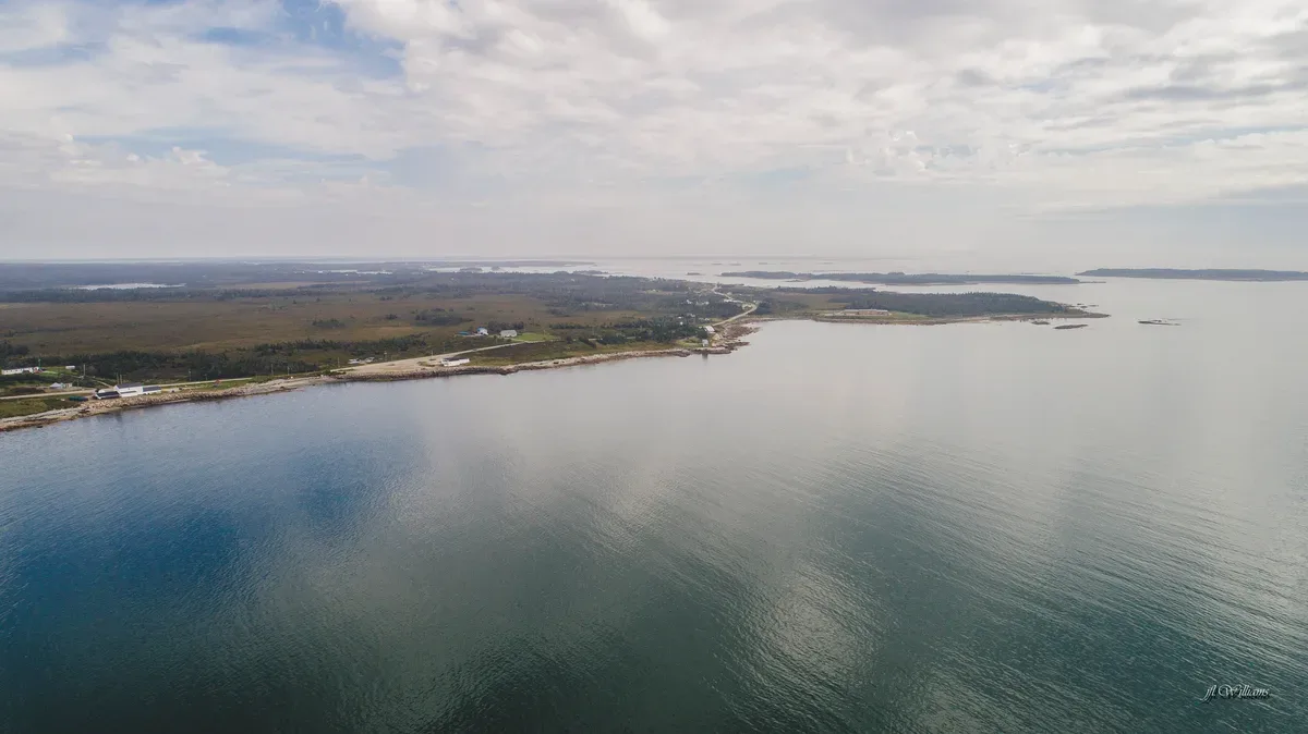 Aerial shot of a small fishing harbor with wooden wharves, moored boats, and a rocky shoreline surrounded by dark sea