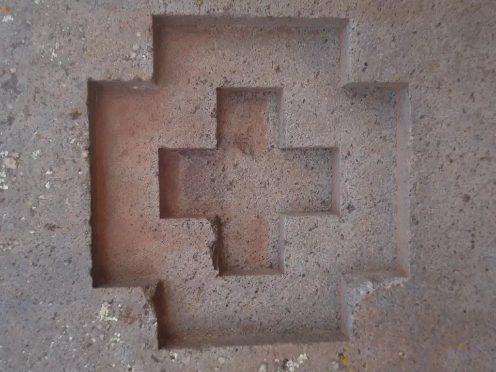 Close-up detail of a perfectly carved recessed stepped cross, known as a Chakana, in hard stone, demonstrating the extreme precision of Puma Punku's builders