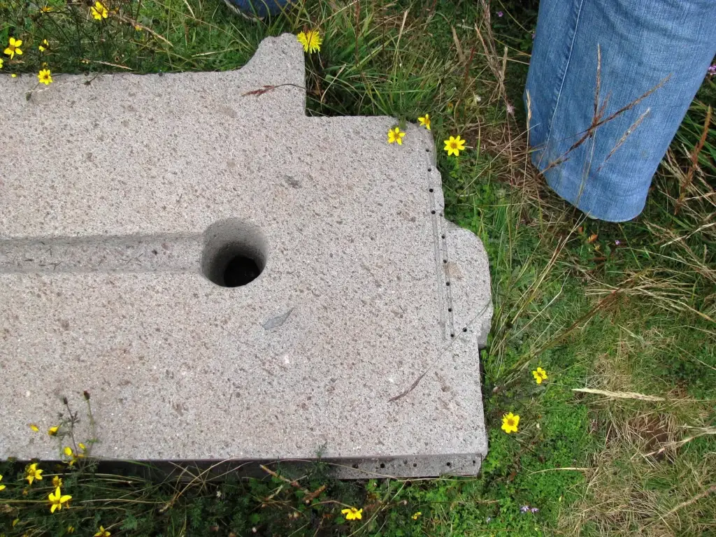 Close-up of a stone block at Puma Punku featuring a straight channel, a circular hole, and a row of small, evenly spaced drilled holes along the edge