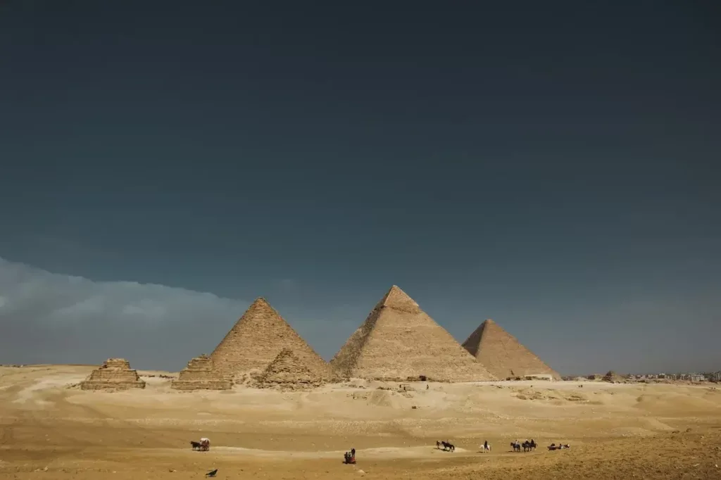 The pyramids of Giza under a dark, stormy sky, with smaller queens' pyramids in the foreground